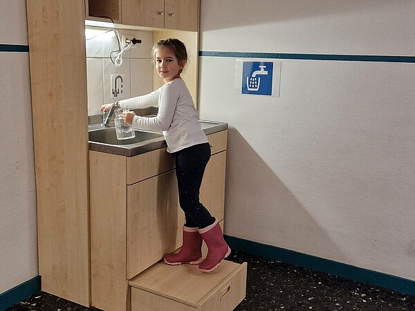 Kind zapft sich Wasser am Wasserspender der Kita