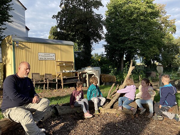 Kinder und KiTa-Leiter sitzen im Kreis auf dem Acker