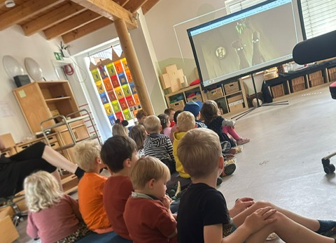 Kinder sitzen vor Leinwand in der KiTa